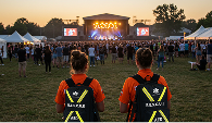 Two female Mosaic Medical employees wearing their orange uniform and a black backpack with highlighter yellow reflective lines. RESCUE and AED is prominent on the face of the bag.