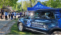 A Mosaic Medical vehicle parked beside a Mosaic Medical tent at an outdoor event at a park.