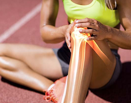 A woman in athletic wear sits on a track, holding her knee with a painful expression. An overlay highlights the knee joint, indicating injury.