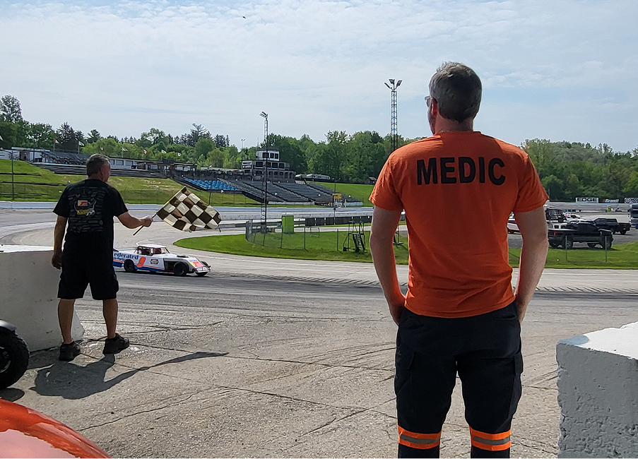 A Mosaic Medical medic standing by at a motorsport event behind concrete barriers.