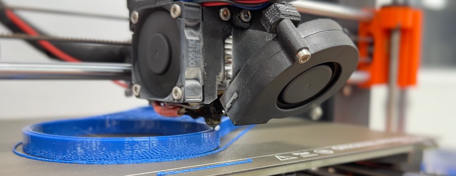 A 3D printer nozzle is depositing blue filament, creating a circular object on the printer bed.